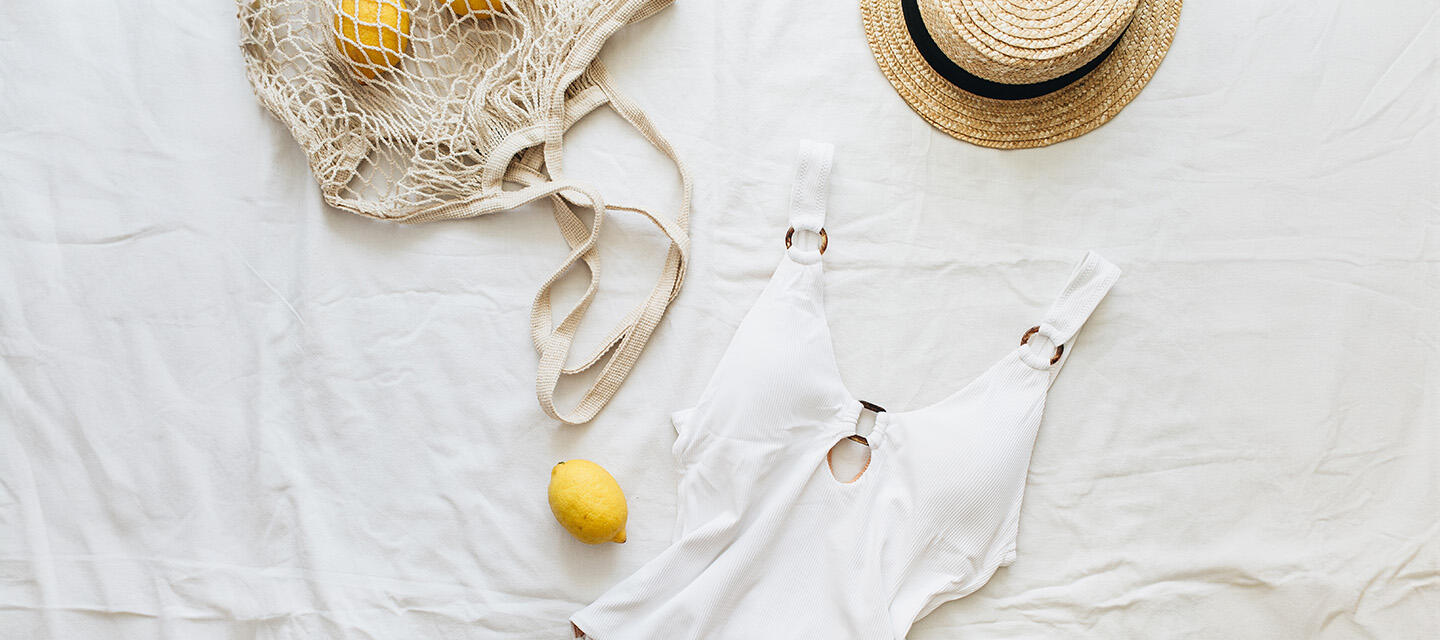 White swimsuit, straw hat, and a natural bag with lemons on a white sheet